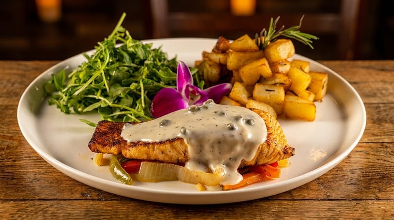 Grilled salmon with creamy sauce, roasted potatoes, and a fresh green salad on a white plate.