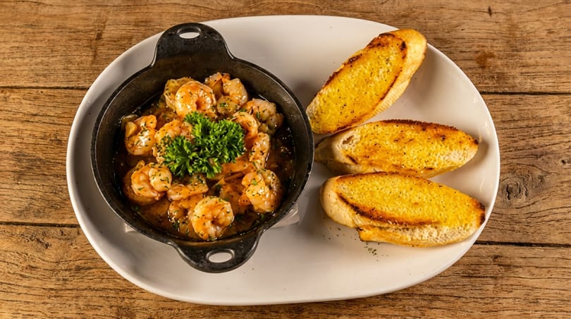 Shrimp scampi in a black skillet with parsley, served with three slices of garlic bread.