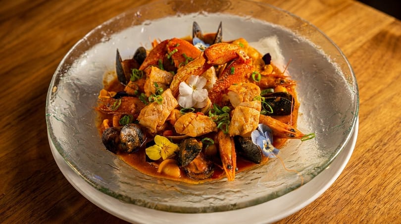 Seafood stew with crab, shrimp, mussels, and white fish, garnished with edible flowers and scallions.