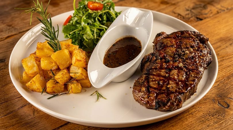 Grilled steak with roasted potatoes, a side salad, and a gravy boat on a white plate.